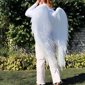 Puede incluir: Grandes alas de ángel blancas con estructuras superpuestas en forma de plumas puntiagudas y un acabado sutilmente brillante. Las alas están diseñadas para llevarse en la espalda, extendiéndose desde los hombros hasta la parte baja de la espalda.