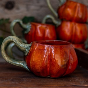 May include: A set of four ceramic pumpkin mugs with green handles. The mugs are a deep orange color and have a glossy finish.