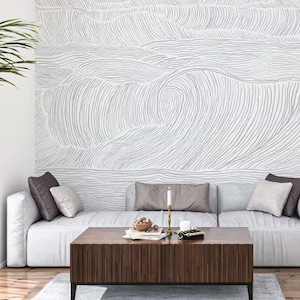 May include: A wall mural featuring a continuous line drawing of ocean waves in gray on a white background. The mural covers the entire wall behind a light gray sofa, creating a textured visual effect that spans the width of the living space.