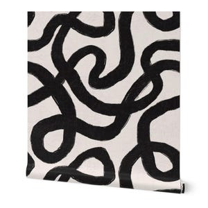 May include: A roll of wallpaper featuring a repeating pattern of thick, black, abstract lines against a cream-colored background. The lines are uneven and create a dynamic, artistic design. The wallpaper is rolled up, showing the edge.