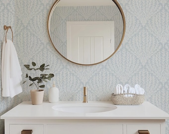 May include: A white bathroom vanity with a sink, a gold faucet, and bronze hardware. Above it, a round mirror with a gold frame hangs on a wall covered in light blue and white botanical wallpaper. A white towel, a plant, and a basket are present.