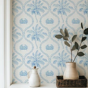 May include: Wallpaper featuring a repeating pattern of blue crabs and palm trees on a white background. The design includes an intricate lattice of leafy vines framing each crab and palm tree motif, creating a coastal aesthetic for interior walls.