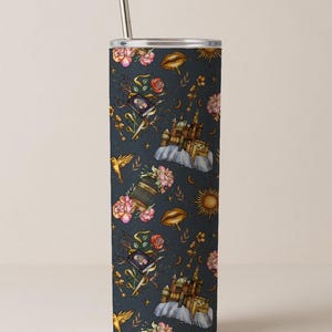 May include: A stainless steel tumbler with a whimsical pattern of castles, birds, flowers, and celestial elements in shades of gold, pink, and blue. The design is set against a dark blue background. Includes a silver straw.