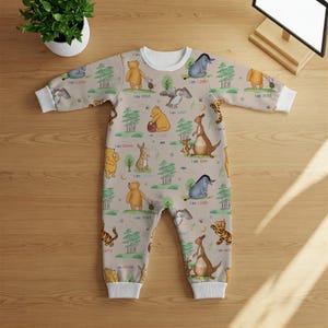 May include: A beige baby onesie with a white trim. The onesie features a repeating pattern of Winnie the Pooh characters, including Tigger, Eeyore, Piglet, and Pooh Bear. Each character has a phrase printed below it, such as "I am loved", "I am brave", and "I am strong".