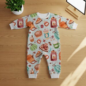 Op de afbeelding: Een witte baby romper met een blauw-wit ruitjespatroon. De romper is bedekt met een aquarelprint van herfstthema's, waaronder pompoenen, taart, koffie en kaneelstokjes.