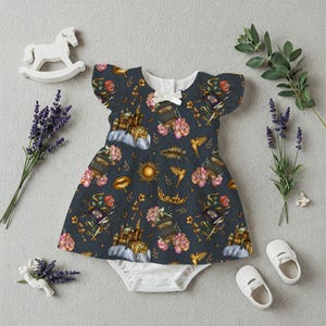 May include: A dark blue baby dress with a whimsical pattern of castles, flowers, birds, and suns. The dress has flutter sleeves and a white bow at the neckline. White baby shoes and a rocking horse are also in the image.
