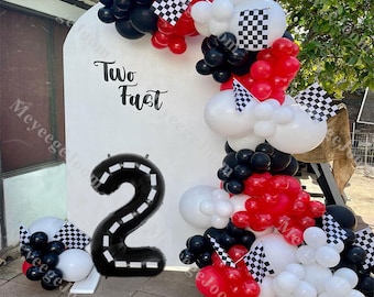 May include: A black and white checkered balloon arch with red and white balloons. The arch is decorated with black and white checkered flags. A large black number 2 balloon with a white checkered road design is in front of a white backdrop with the words "Two Fast" written on it.