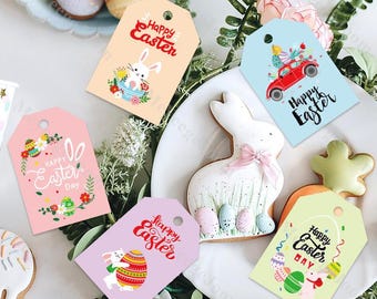 May include: A collection of colorful Easter gift tags with various designs, including bunnies, eggs, and the text "Happy Easter." The tags are in shades of pink, blue, and yellow, and are arranged on a white plate with Easter-themed cookies.