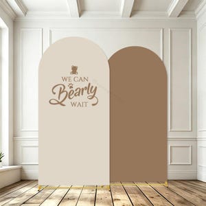 Peut inclure: Deux panneaux de fond en forme d'arche avec une finition lisse. Le panneau de gauche est beige clair avec un motif marron représentant un ours en peluche, une empreinte de patte et le texte "WE CAN Bearly WAIT". Le panneau droit est marron.