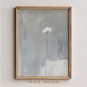 May include: A framed art print depicting a single white flower on a long stem against a muted blue and grey background. The artwork is in a wooden frame and has a minimalist aesthetic. The text "WALL AFFAIR" is at the bottom.