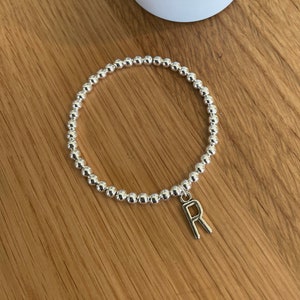May include: A silver beaded bracelet with a silver charm in the shape of the letter R.