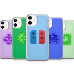 May include: Five different phone cases with various gaming controller designs. The cases are clear and show the phone's camera lens. The designs include a purple case with PlayStation controller buttons, a green case with Xbox controller buttons, a blue case with Nintendo Switch Joy-Con controllers, a blue case with a generic gamepad, and a green case with a Pac-Man maze.