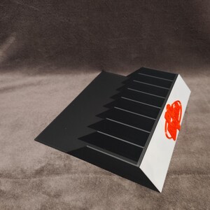 Peut inclure: Organisateur en plastique noir et blanc avec un logo rouge. L'organisateur a sept fentes pour ranger des objets.