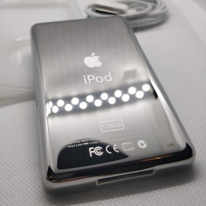 May include: A silver iPod with the Apple logo and the text "iPod" on the front. The back of the device has the text "128GB" and various certifications including FCC, CE, and VCI.