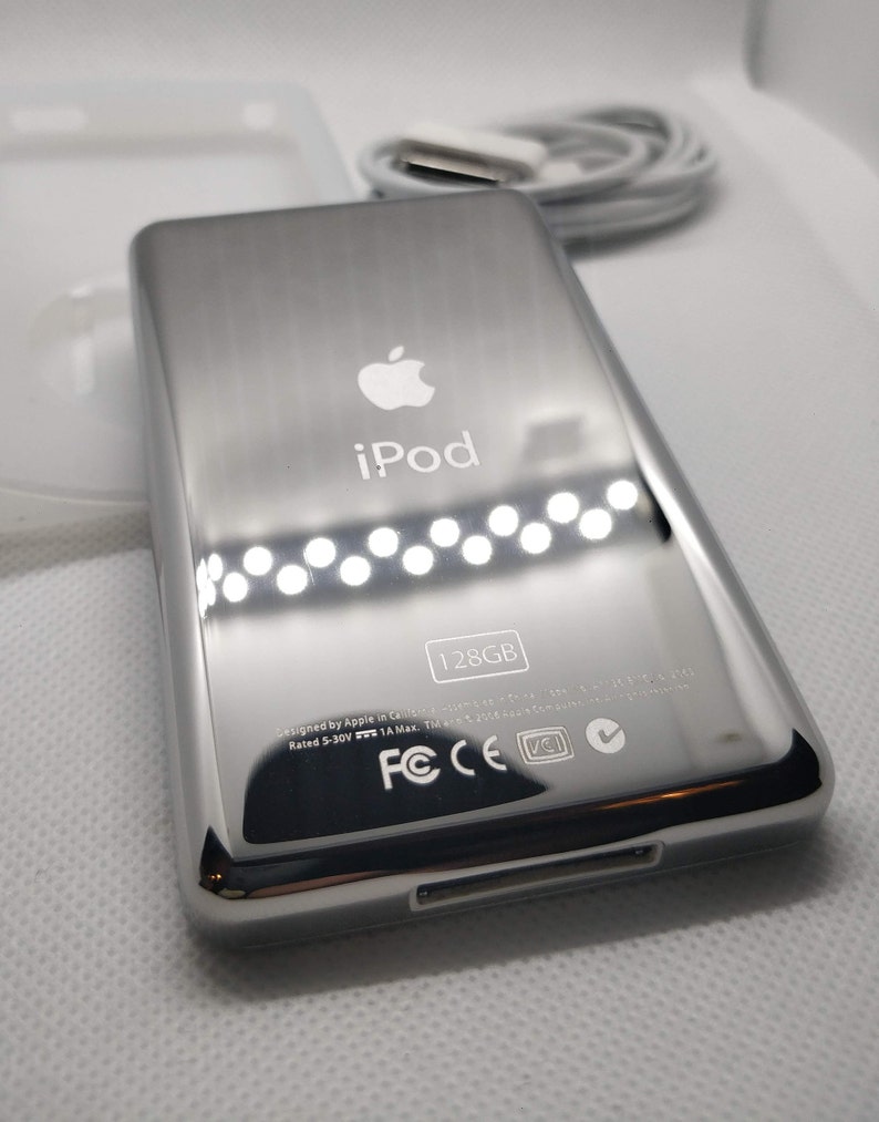 May include: A silver iPod with the Apple logo and the text "iPod" on the front. The back of the device has the text "128GB" and various certifications including FCC, CE, and VCI.