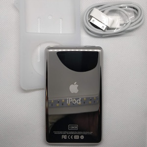 May include: A silver iPod with a white front and a black screen. The iPod has a white Apple logo and the word "iPod" in white letters. The iPod is 128GB and has a white USB cable. The iPod is in a white silicone case.