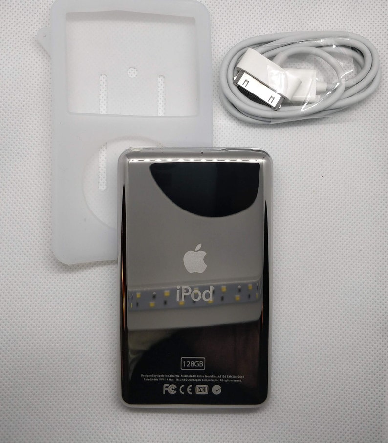 May include: A silver iPod with a white front and a black screen. The iPod has a white Apple logo and the word "iPod" in white letters. The iPod is 128GB and has a white USB cable. The iPod is in a white silicone case.