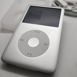 May include: A silver iPod Classic with a black and white screen displaying the song "Lemonade" by Beyonce and The Weeknd. The screen also shows the song is 4:11 long and is track 1 of 624. The iPod has a circular click wheel with play, pause, and skip buttons.