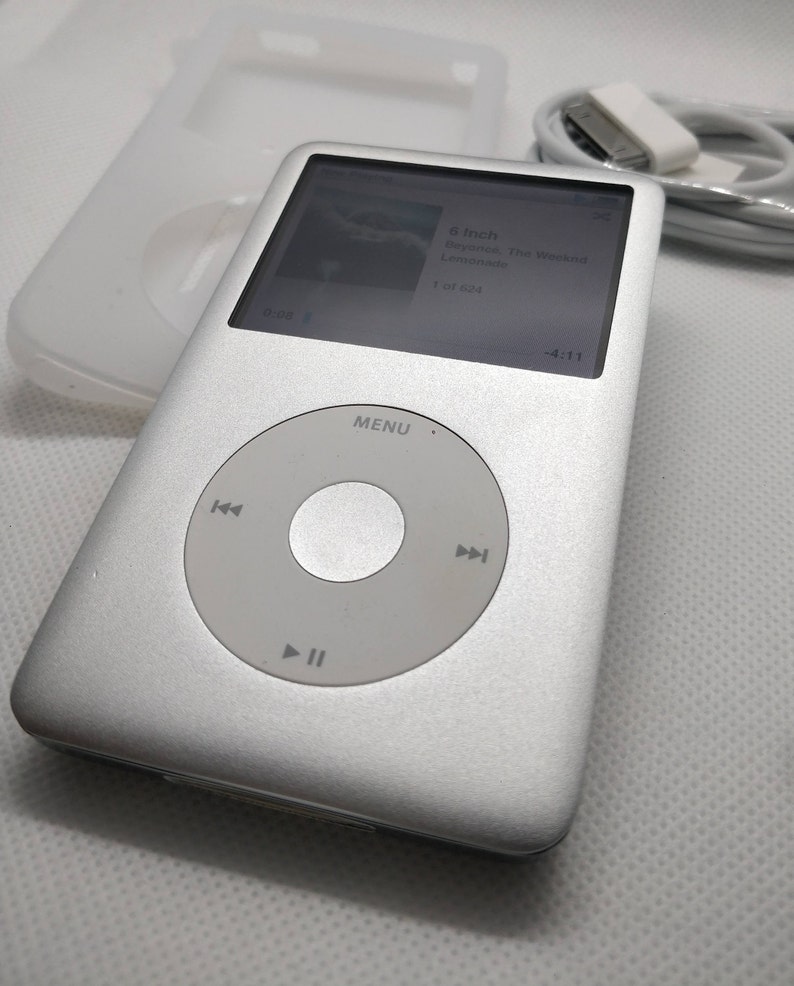 May include: A silver iPod Classic with a black and white screen displaying the song "Lemonade" by Beyonce and The Weeknd. The screen also shows the song is 4:11 long and is track 1 of 624. The iPod has a circular click wheel with play, pause, and skip buttons.