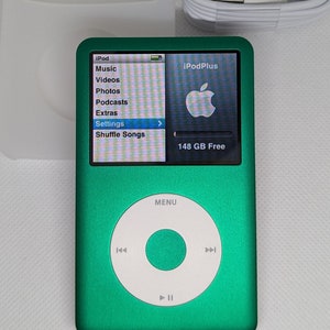 Puede incluir: Un iPod Plus verde con una rueda de clic blanca y una pantalla que muestra "iPod Plus" y "148 GB libres". El iPod tiene un menú con opciones para Música, Vídeos, Fotos, Podcasts, Extras, Ajustes y Reproducción aleatoria de canciones.
