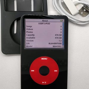 May include: Black iPod with a red control wheel and a screen displaying device information. The screen shows "USER'S IPOD" and details like capacity and version. A white USB cable and a black case are also present.