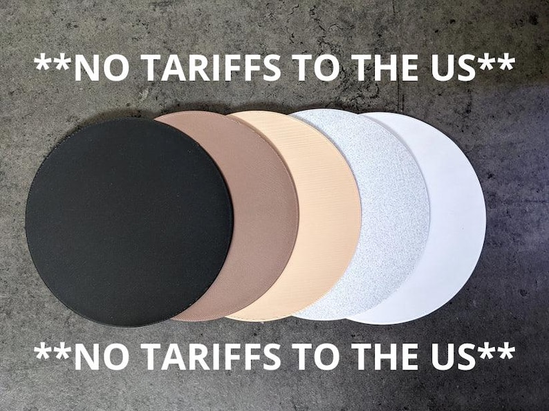 May include: A collection of six circular objects in varying colors: black, brown, beige, off-white with glitter, and white. The text "**NO TARIFFS TO THE US**" is displayed above and below the objects in white.