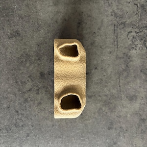 May include: A beige 3D printed object with two holes in the top and one hole in the bottom.