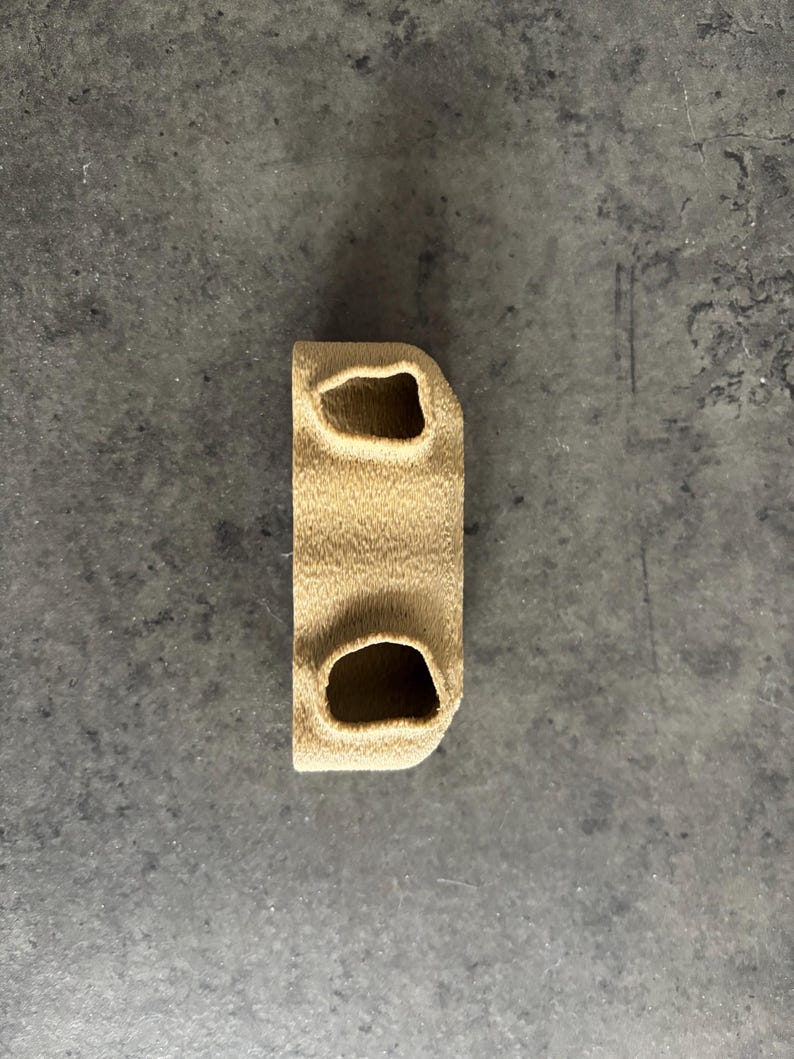 May include: A beige 3D printed object with two holes in the top and one hole in the bottom.