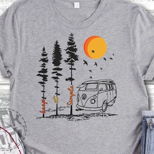 May include: Gray t-shirt with a black and white illustration of a vintage camper van, trees, and a sun. The text "Keep it simple" is written vertically on the left side of the design.