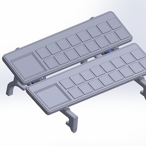 Puede incluir: Dos bandejas grises en ángulo con una cuadrícula de cuadrados pequeños y un cuadrado más grande en cada una. Las bandejas están soportadas por un diseño de patas curvas. El diseño general es de color gris claro.