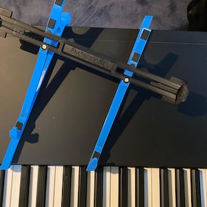 May include: A blue and black keyboard stand with the text "BMStudioNL" printed on it. The stand is designed to hold a keyboard or other device at an angle.