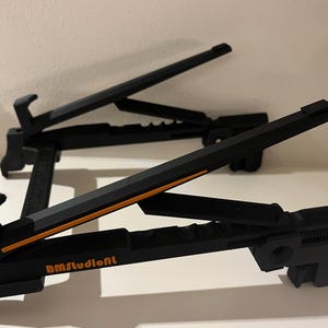 May include: Two black adjustable music stands with orange detailing. The stands are made of a durable material and feature a design that allows for easy adjustment. The stands have the text "BMstudioNL" printed on them.