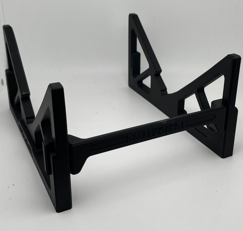 May include: Black, geometric stand with a horizontal support beam. The stand has a triangular design on the sides and a rectangular base. The text "101011101" is printed on the horizontal beam. The stand is designed to hold an item.