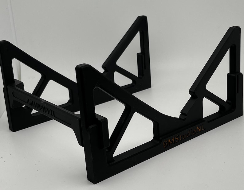 May include: A black, geometric stand with a triangular design. The stand has a rectangular base and angled supports, with the text "BMStudioNL" visible. The stand is designed to hold an item.
