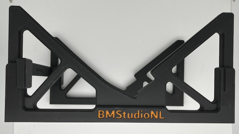 May include: Black, geometric shelf bracket with a triangular design. The bracket has a rectangular base with the text "BMStudioNL" in orange. The bracket is designed to hold items and is set against a white background.