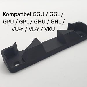 Może przedstawiać: Czarny plastikowy element o prostokątnej podstawie i podwyższonych sekcjach. Na górze wydrukowano tekst "Kompatibel GGU / GGL / GPU / GPL / GHU / GHL / VU-Y / VL-Y / VKU". Element posiada otwór montażowy.