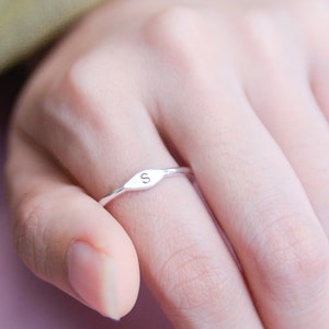 Könnte beinhalten: Ein silberner Ring mit einem kleinen, ovalen Band. Das Band ist mit dem Buchstaben "S" graviert.