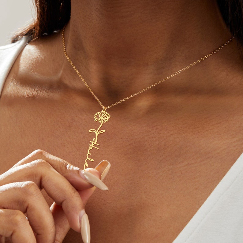 May include: A gold-colored necklace featuring a sunflower design and the name "Halle" in a delicate script. The pendant hangs from a fine chain, creating an elegant and personalized accessory. The necklace is worn around the neck.