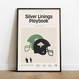 May include: A black and white poster with the title "Silver Linings Playbook" in bold black text. The poster features two football helmets, one green and one black, with a sun and a cloud graphic on each. The poster is framed in a black frame.