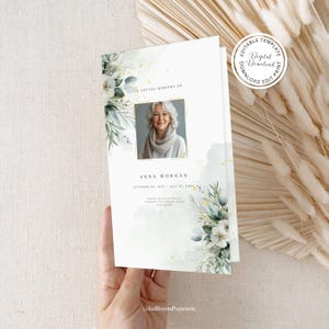 Könnte beinhalten: Eine druckbare Trauerfeier-Vorlage mit einem Aquarell-Blumendesign in Grün- und Weißtönen. Die Vorlage enthält einen Platzhalter für ein Foto, die Worte "In Loving Memory Of" und den Text "Anna Morgan, 08. Oktober 1952 - 07. Mai 2023".