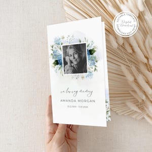 May include: A white funeral program card featuring a black and white portrait of a person surrounded by a watercolor illustration of blue hydrangeas and green leaves. The text reads in loving memory, AMANDA MORGAN, and 13.12.19XX - 11.01.2025.