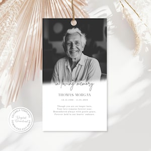May include: A rectangular memorial tag featuring a black and white portrait of an elderly person at the top. Below the photo, the text reads in loving memory, THOMAS MORGAN, 13.12.1950 - 11.01.2025, and a short poem. The tag has a hole at the top.