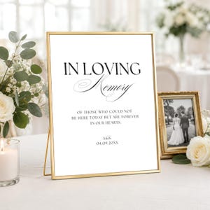 May include: A gold-framed sign with white background and black text reading IN LOVING MEMORY OF THOSE WHO COULD NOT BE HERE TODAY BUT ARE FOREVER IN OUR HEARTS. A&K 04.09.20XX is printed at the bottom. The sign is displayed in a thin metallic frame.