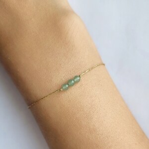 Könnte beinhalten: Ein zartes Armband aus einer goldenen Kette mit drei kleinen, runden, hellgrünen Perlen.