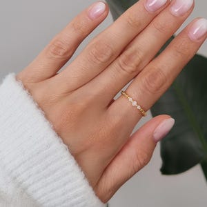 Könnte beinhalten: Ein goldener Ring mit drei kleinen, runden, hellrosa Steinen. Der Ring befindet sich an einem Finger, mit einem weißen Ärmel im Eck. Die Nägel sind mit einem hellrosa Farbverlauf lackiert.