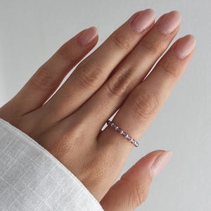 Könnte beinhalten: Ein zarter Ring mit einem sich wiederholenden Muster aus kleinen, runden, hellvioletten Amethystperlen, die mit winzigen, polierten, silberfarbenen Metallzwischenperlen durchsetzt sind und ein schlichtes, durchgehendes Ringdesign bilden.