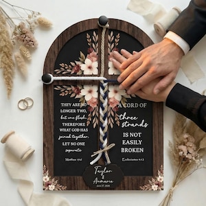 Può includere: Un cartello di nozze in legno con cornice scura e sfondo nero. Il cartello presenta accenti floreali, un design a corda intrecciata e il testo "A Cord of Three Strands Is Not Easily Broken". Sono inclusi anche i nomi "Taylor & Annmarie" e la data.