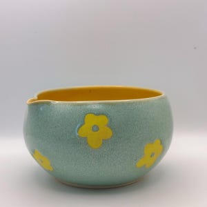 Może przedstawiać: Niebieska ceramiczna miska z ż&oacute;łtym rantem i ż&oacute;łtymi wzorami kwiat&oacute;w.