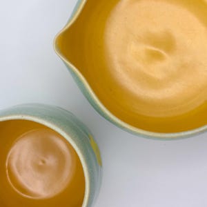 Może przedstawiać: Dwie ceramiczne miski z jasnoniebieską glazurą i ż&oacute;łtym wnętrzem. Miski są włożone w siebie, większa miska jest na g&oacute;rze.