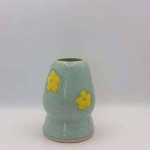 Może przedstawiać: Jasnoniebieski ceramiczny wazon z zaokrągloną podstawą i dwoma ż&oacute;łtymi wzorami kwiat&oacute;w.